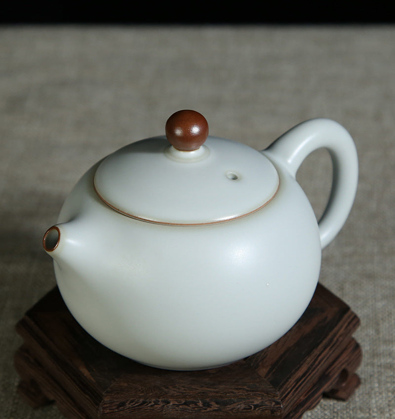 The picture of the teapot with moon-white glaze of Ru Kiln. The body of the teapot has smooth and elegant lines, being round and full, showing a simple, unsophisticated and magnificent modeling style. Its moon-white glaze is like the first snow in winter, with a slight bluish-gray tint in the whiteness, emitting a soft luster under the light, giving people a sense of coolness and elegance. The spout and the handle of the teapot are exquisitely designed with a harmonious proportion, perfectly integrating wit